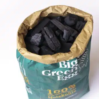Ein geöffneter Sack der Big Green Egg Holzkohle, neben einem Haufen schwarzer Holzkohle, steht für Qualität und Nachhaltigkeit, um ein unübertroffenes Grillaroma zu bieten.