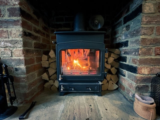 Ein rustikaler Kaminofen eingebettet in altes Ziegelmauerwerk, brennend mit trockenem und hochwertigem Brennholz von Kaminholz Breuer, bereit für warme und gemütliche Abende zu Hause.